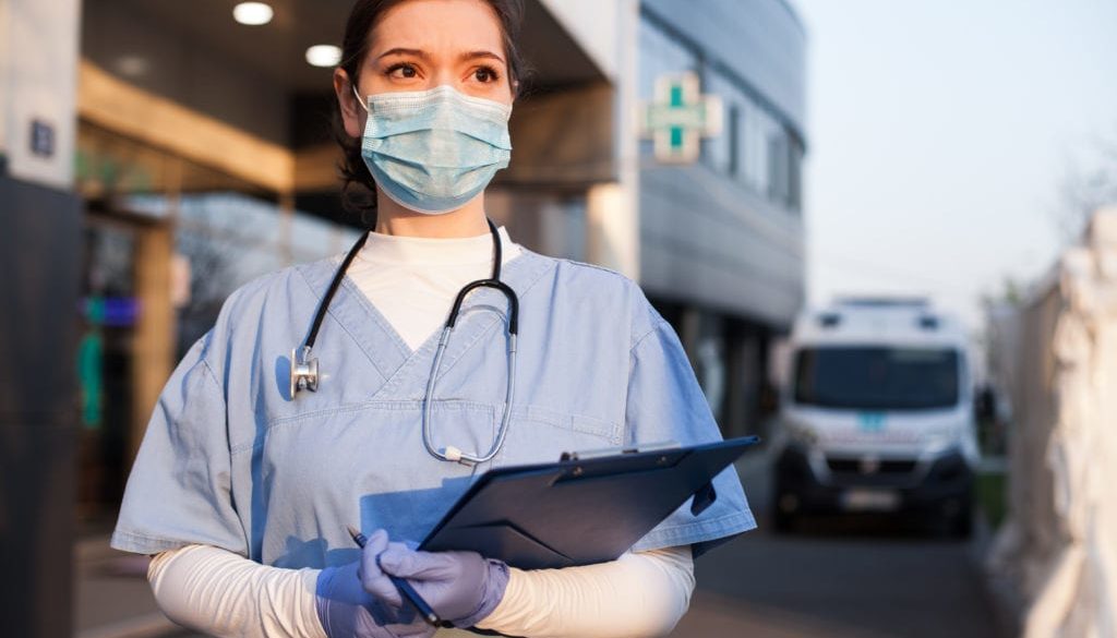 healthcare worker wearing mask standing in front of hospital